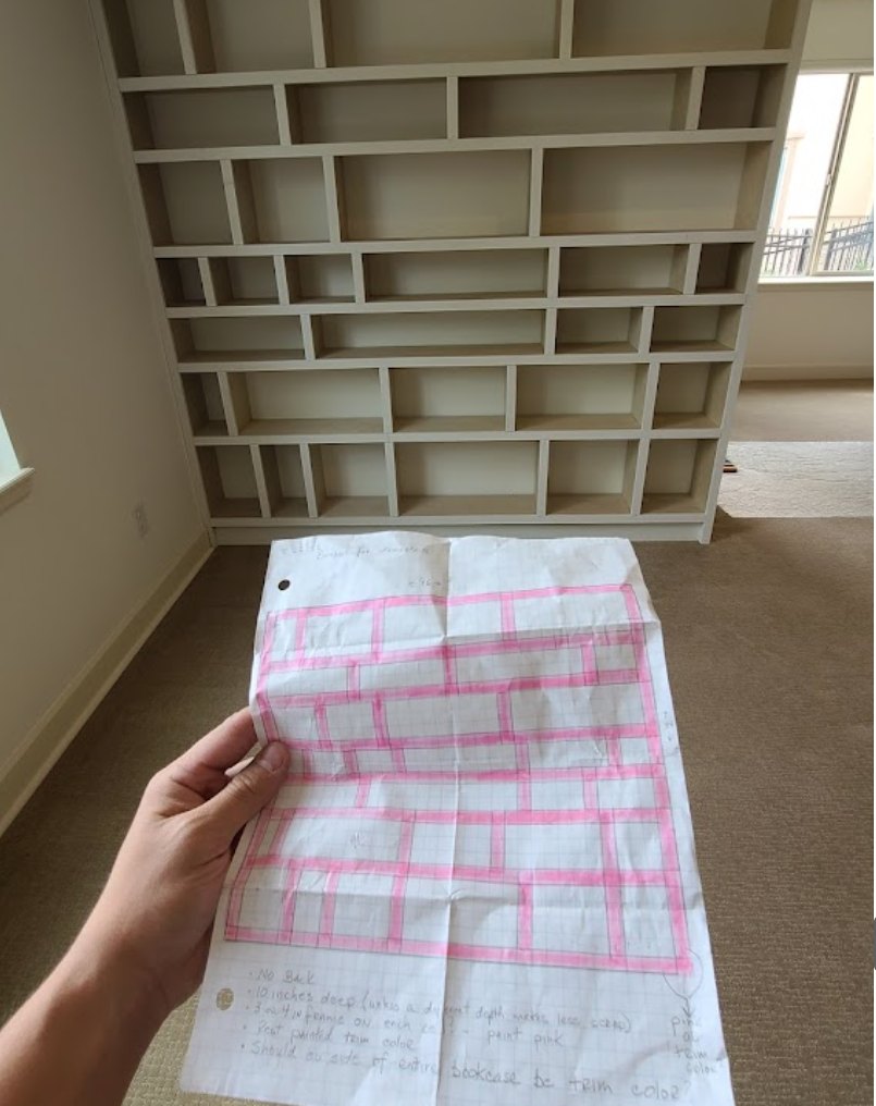 Hand-drawn shelf layout held up in front of the matching built-in bookcase under construction
