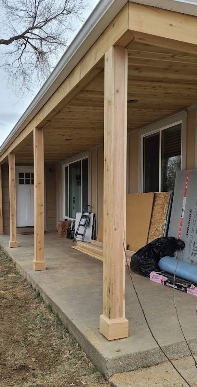 Cedar porch posts and plank soffit along a covered front porch, mid-build