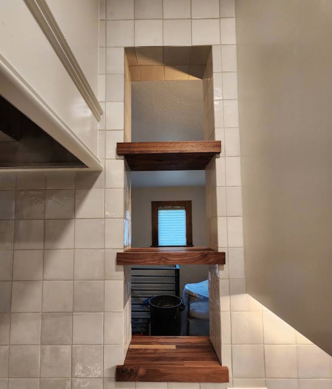 Walnut floating shelves stacked in a tiled pass-through niche